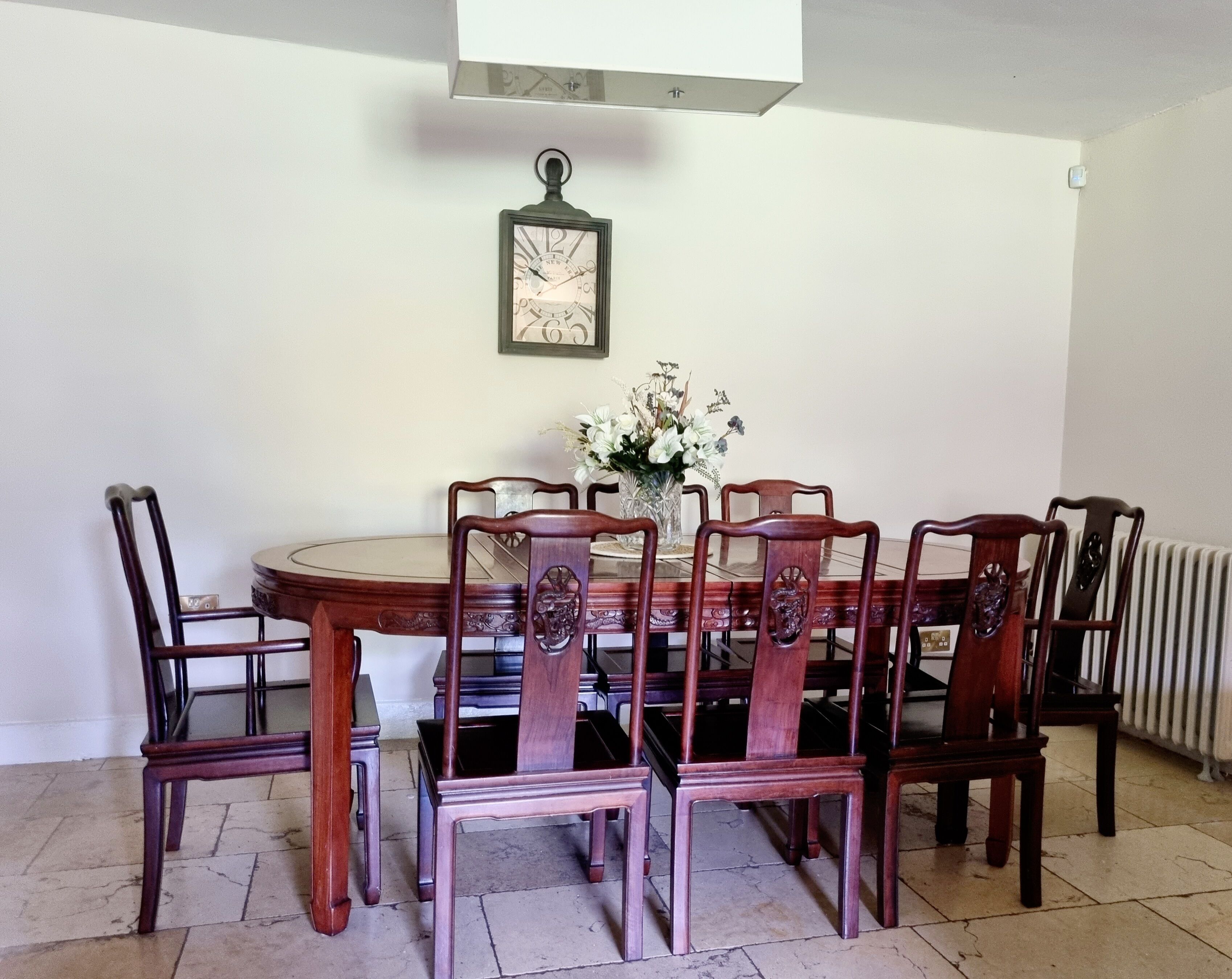 Un coin repas avec une table ronde, six chaises en bois et une horloge fixée au mur.