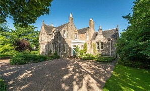 A stone building with a gravel driveway and lush greenery.