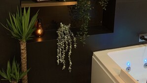 Un baño moderno con un espejo grande, una bañera y varias plantas en estantes.