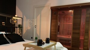 Una cama bien hecha con una mesita de noche de madera, una planta pequeña en maceta y un objeto negro sobre la mesa.