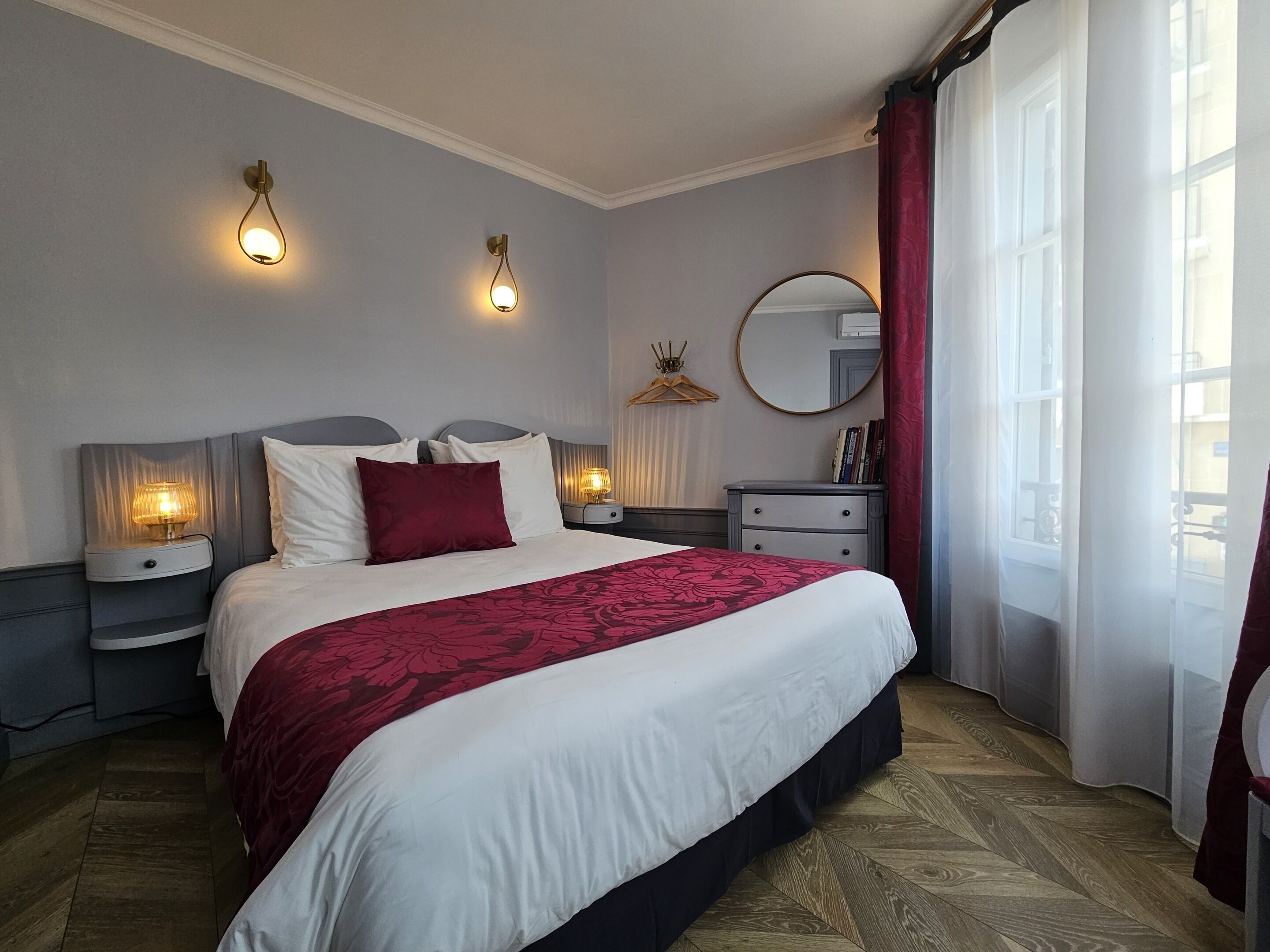 Une chambre à coucher bien aménagée, avec un grand lit, des tables de chevet, une commode, un miroir et deux lampes fixées au mur.