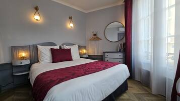 Une chambre à coucher bien aménagée, avec un grand lit, des tables de chevet, une commode, un miroir et deux lampes fixées au mur.