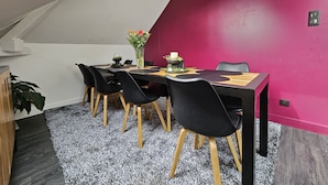 Un comedor con una mesa dispuesta para seis, rodeado de sillas negras con patas de madera, un jarrón con flores y una vela sobre la mesa.
