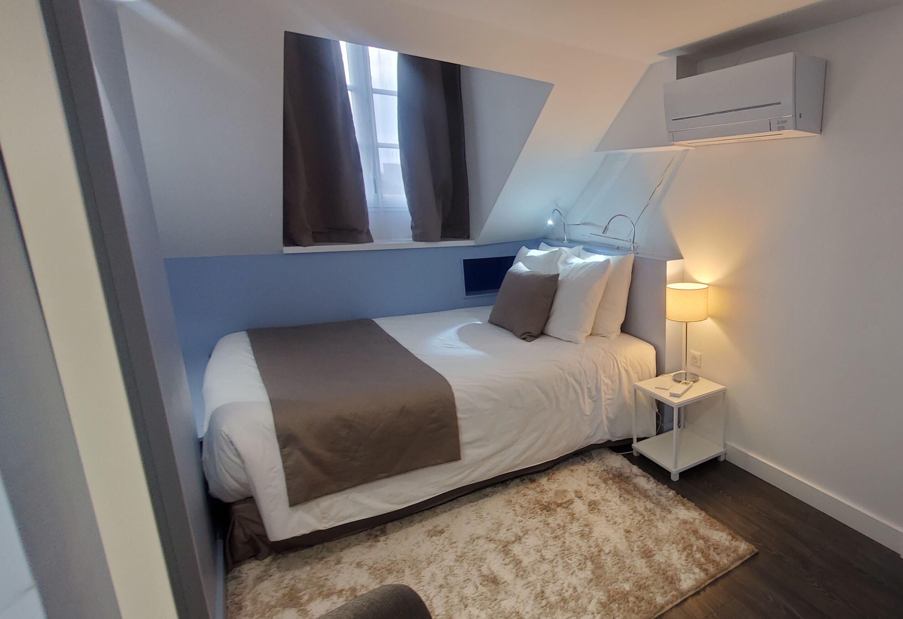 A bedroom with a bed, a nightstand, a lamp, a window with curtains, and a ceiling fan.