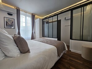 A modern bedroom with a large bed, a walk-in closet, and a large window with curtains.
