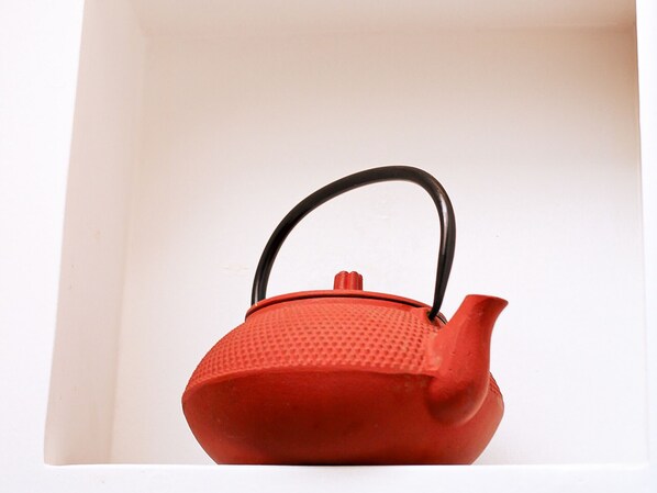 A red teapot with a black handle in a white interior space.