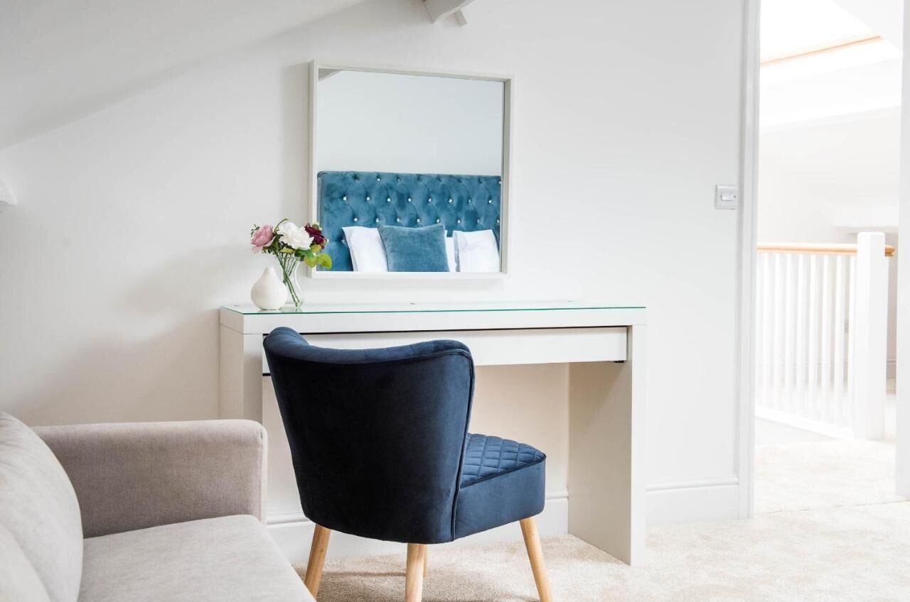 A modern bedroom with a glass desk, a dark blue chair, and a tufted headboard.