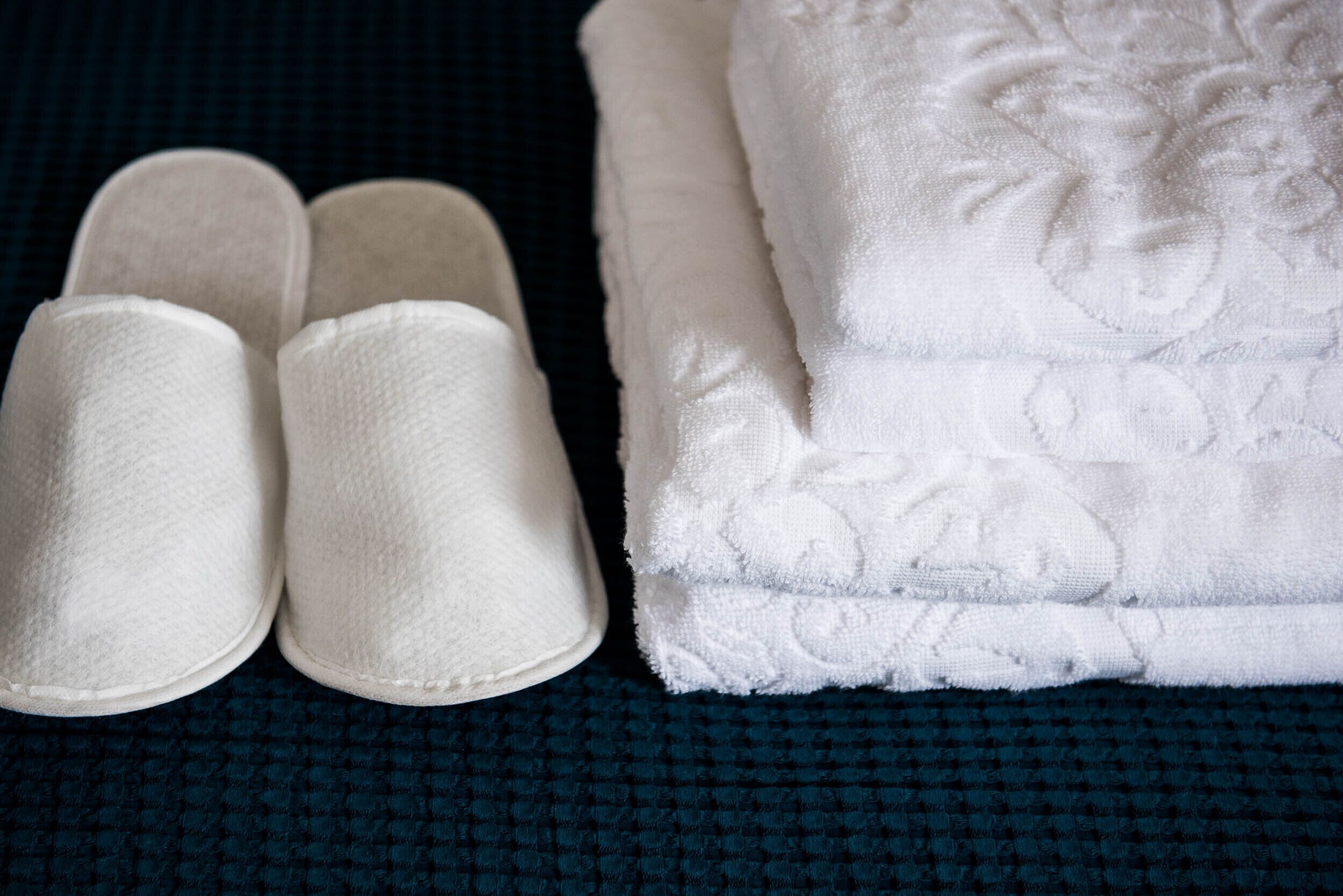 Un par de pantuflas blancas y una toalla blanca doblada sobre una superficie azul oscuro con textura.