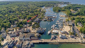 Vue aérienne d’une ville côtière avec un port de plaisance, des maisons et une zone boisée.