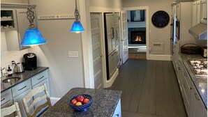 Une cuisine moderne avec des armoires blanches, des comptoirs en granit, un luminaire suspendu bleu et une cheminée.
