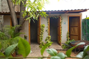 A small building with two wooden doors and a small garden area with a tree and potted plants. - La Casona Hostel (Puerto Escondido)