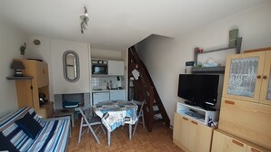 Un espacio habitable compacto con kitchenette, comedor, televisor y escalera.