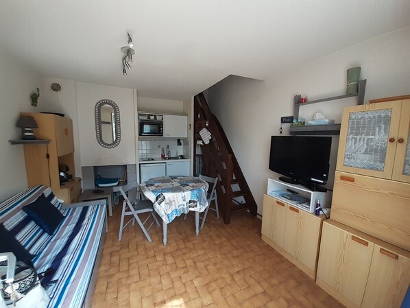 A compact living space with a kitchenette, a dining area, a television, and a staircase.