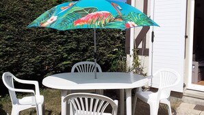 Un patio con una mesa y sillas, un paraguas colorido y una casa al fondo.