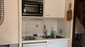 Cocina compacta con microondas integrado, lavaplatos y fregadero.