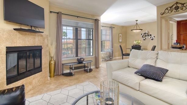 A living room with a fireplace, a sofa, a TV mounted on the wall, and a dining area with a table and chairs.