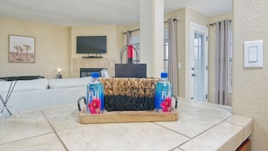 A living room with a sofa, a fireplace, a television, and a tray with two bottles of Fiji water.