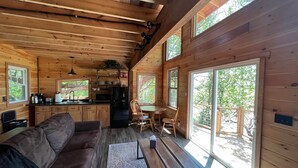 A cozy cabin interior with a wooden interior, a sofa, a dining table, and a kitchen area. - Sunset Reset TreeHouse (Darlington)