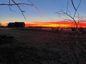 A rural landscape with a house and open fields during sunset.
