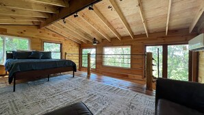 A bedroom with a bed, a bench, and a window with a view of trees. - Sunset Reset TreeHouse (Darlington)