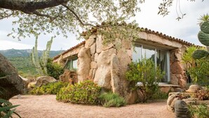 A rustic stone house with large windows, surrounded by cacti and desert plants. - Domaine de Piscia (Figari)