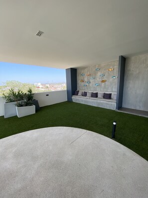 Une terrasse sur le toit avec un revêtement d’herbe artificielle, un espace salon avec des coussins et des décorations murales représentant des poissons.