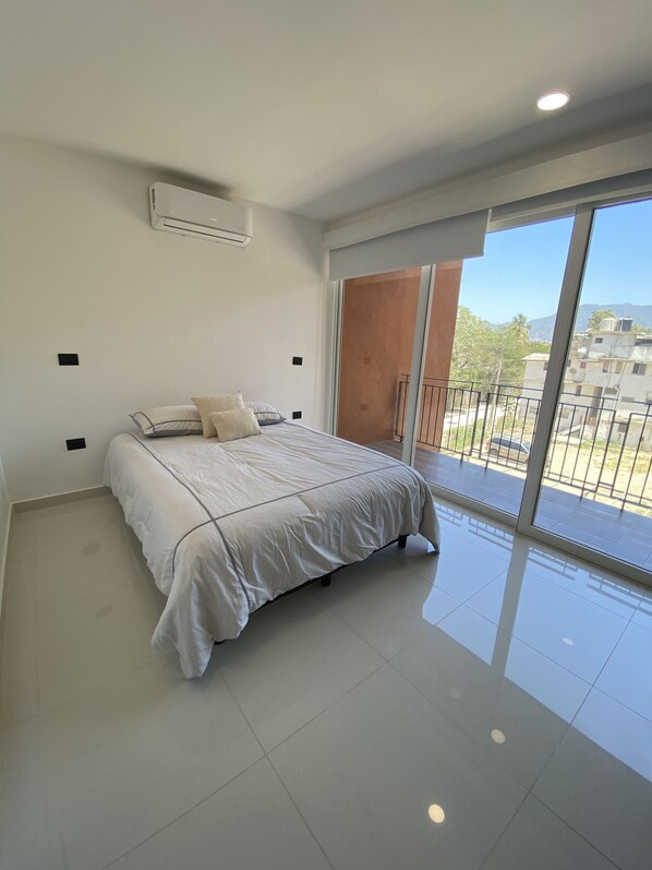 Une chambre avec un lit, une porte-fenêtre coulissante donnant sur un balcon et un climatiseur fixé au plafond.