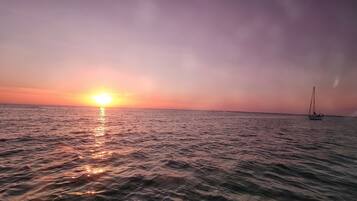Ein Sonnenuntergang über einem ruhigen Meer, im Hintergrund ein Segelboot.