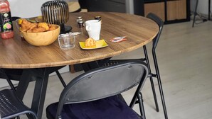 Et spisebord med en skål kager, en juiceflaske og en kop. Der er klapstole og et fjernsyn i baggrunden.