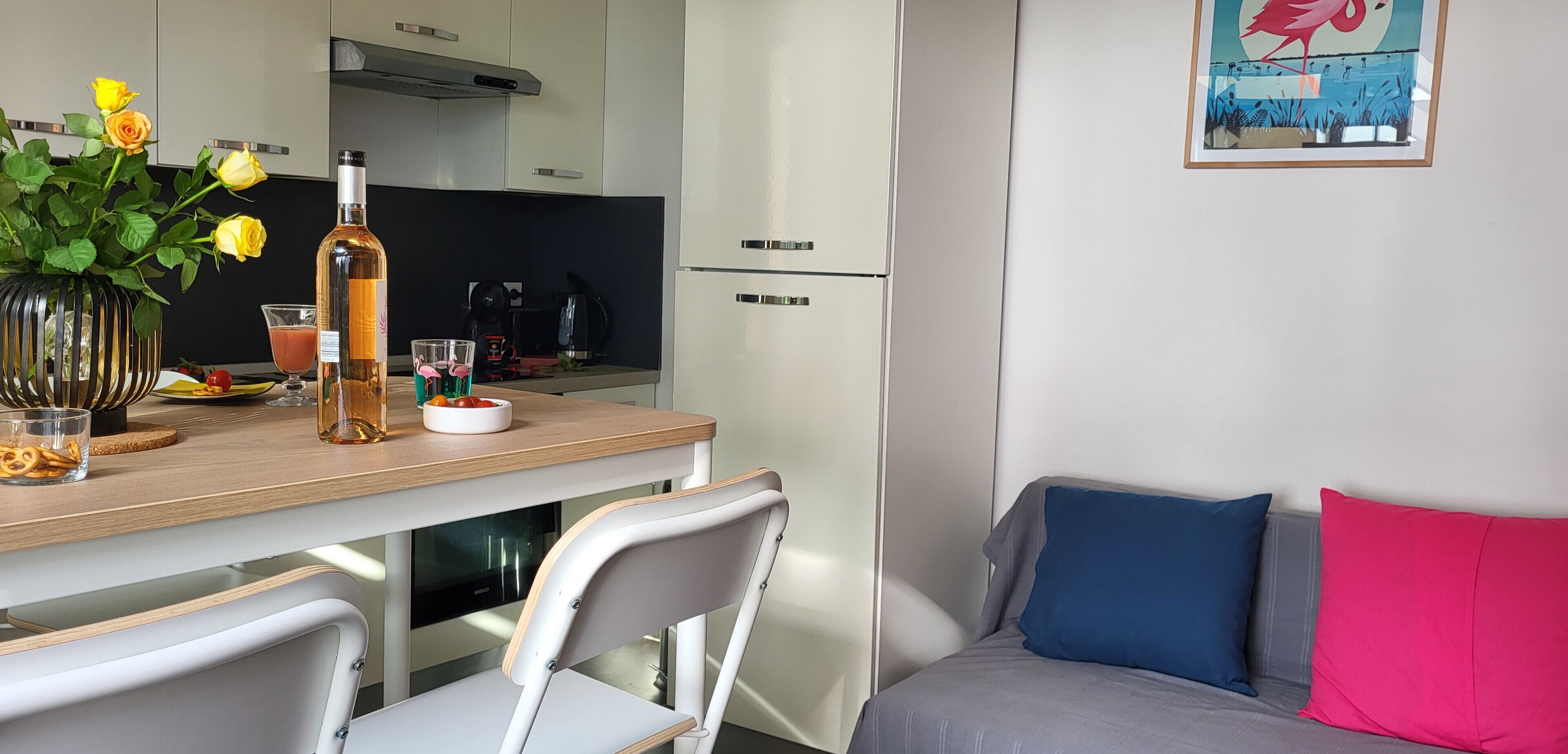 Una cocina moderna con una mesa de comedor, sillas, un florero con flores, una botella y un vaso de bebida.