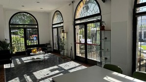 Une pièce spacieuse dotée de grandes fenêtres en arc de cercle, d’un sol en marbre et d’une table entourée de chaises.