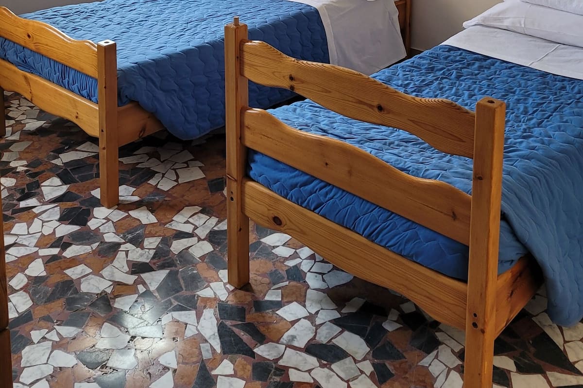 Een kamer met twee houten bedden, een raam met gordijnen en een betegelde vloer.