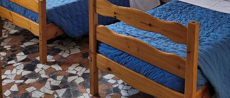 A room with two wooden beds, a window with curtains, and a tiled floor.
