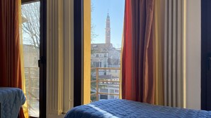 Une chambre d’hôtel avec deux lits, de grandes fenêtres avec des rideaux et une vue sur un immeuble doté d’une tour.