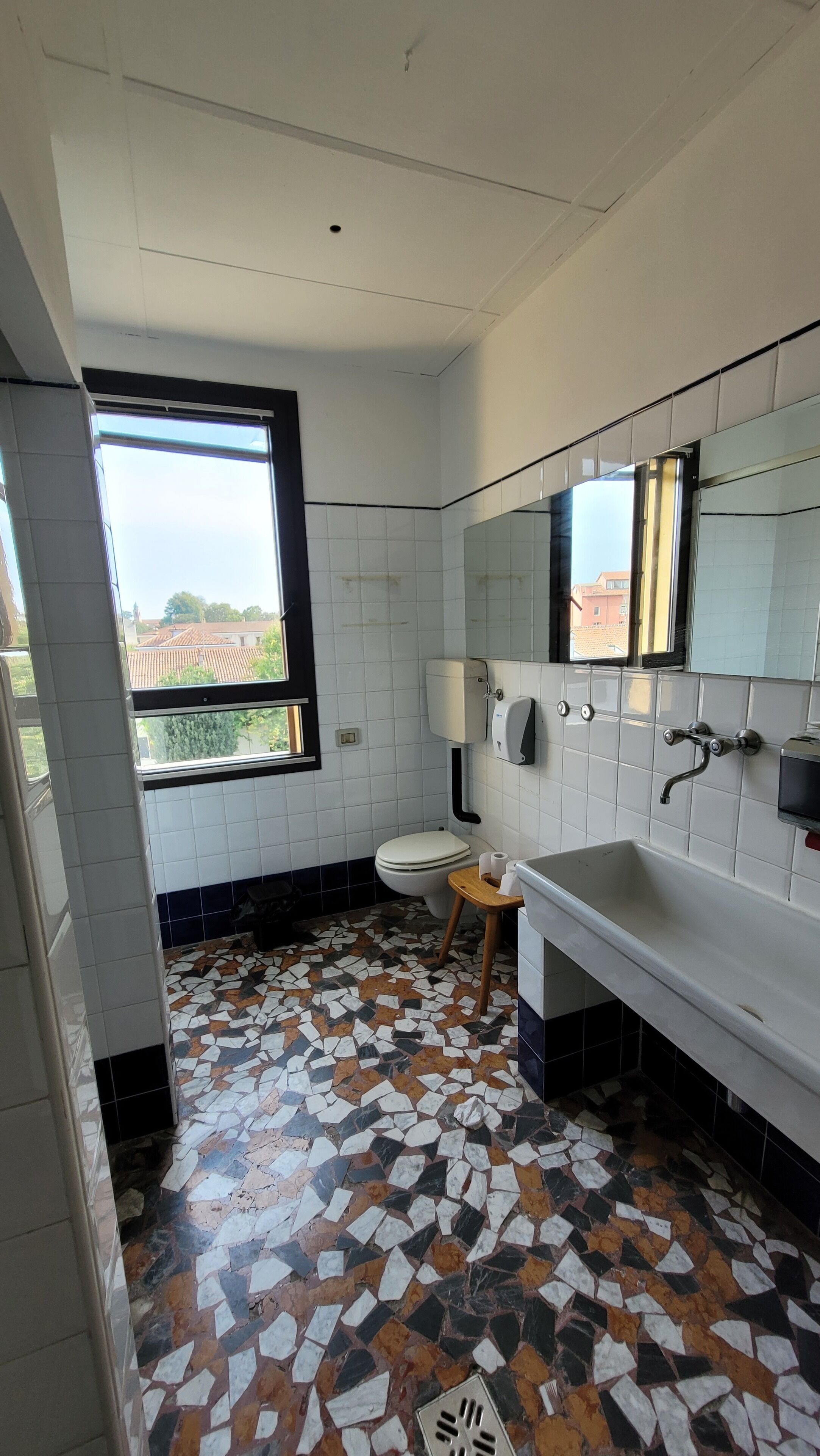 A bathroom with a tiled floor, a toilet, a sink, a mirror, and a window.