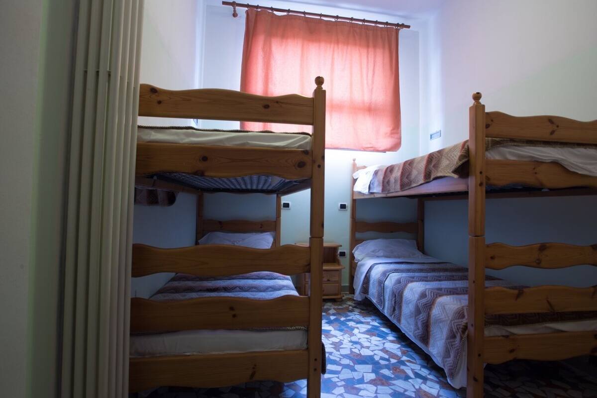 Een studentenkamer met stapelbedden, een raam met gordijnen en een betegelde vloer.