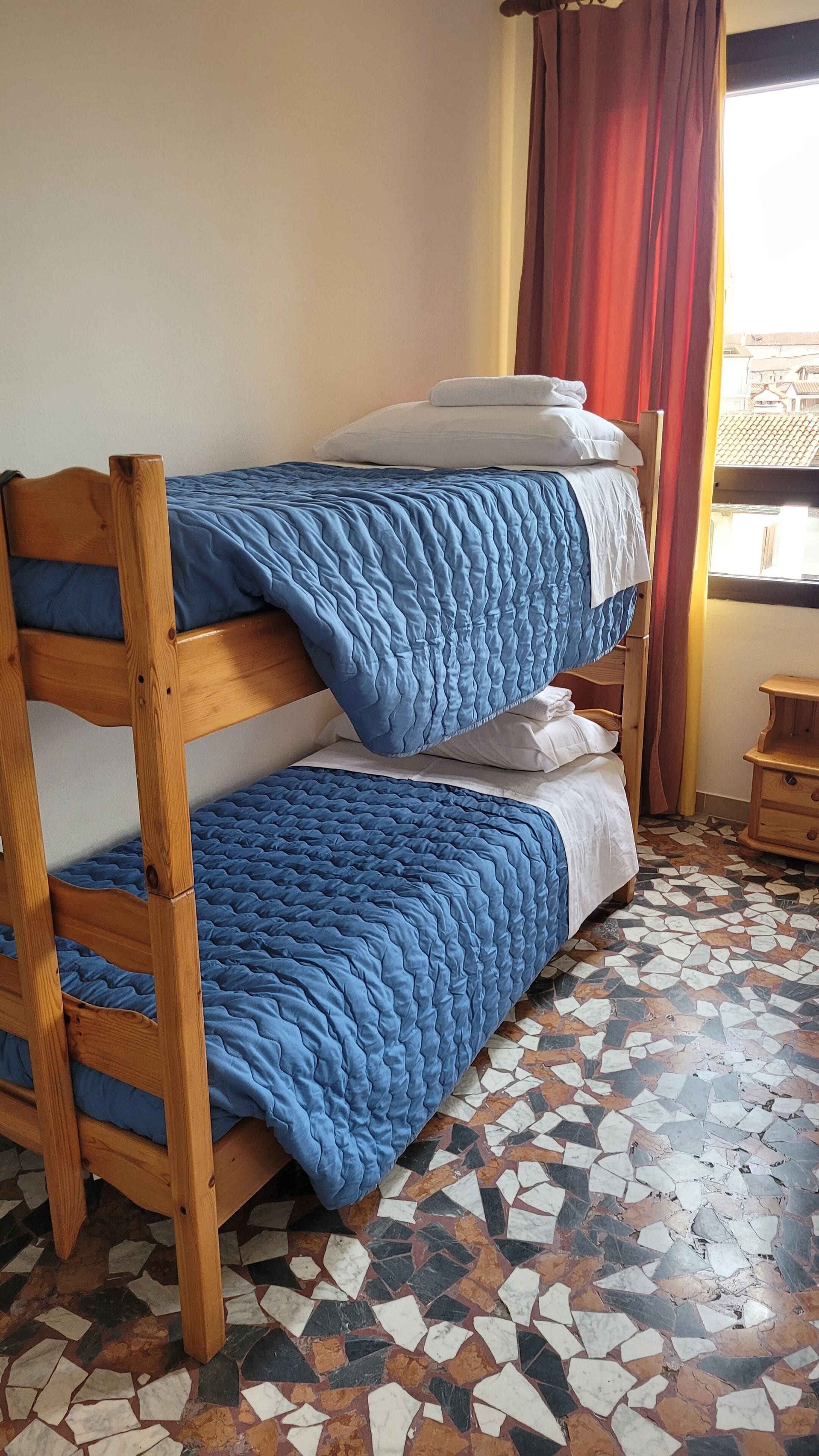 Un lit superposé avec une literie bleue, une tête de lit en bois et un sol carrelé.