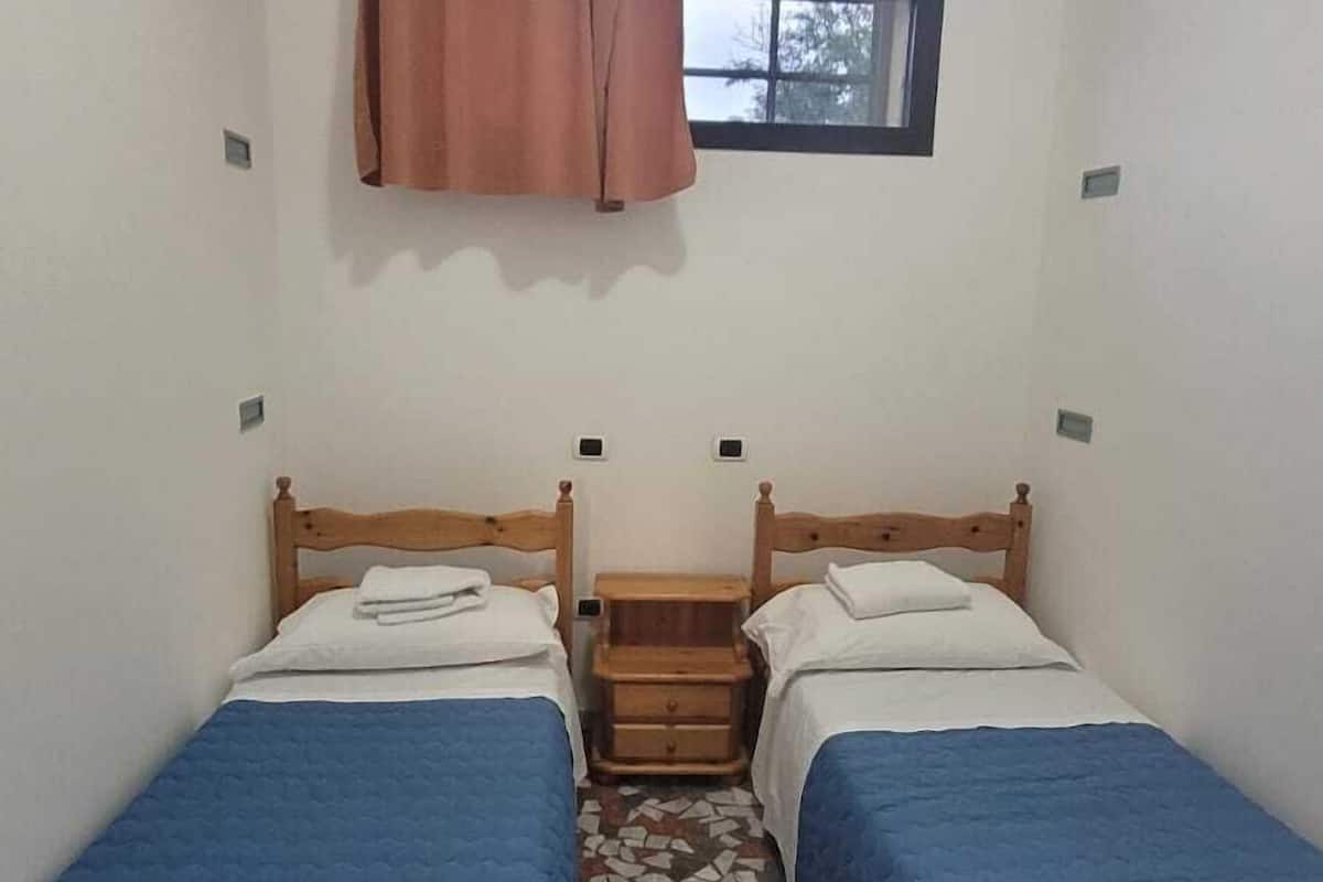 Een kleine kamer met twee houten bedden, een raam met gordijn en een betegelde vloer.