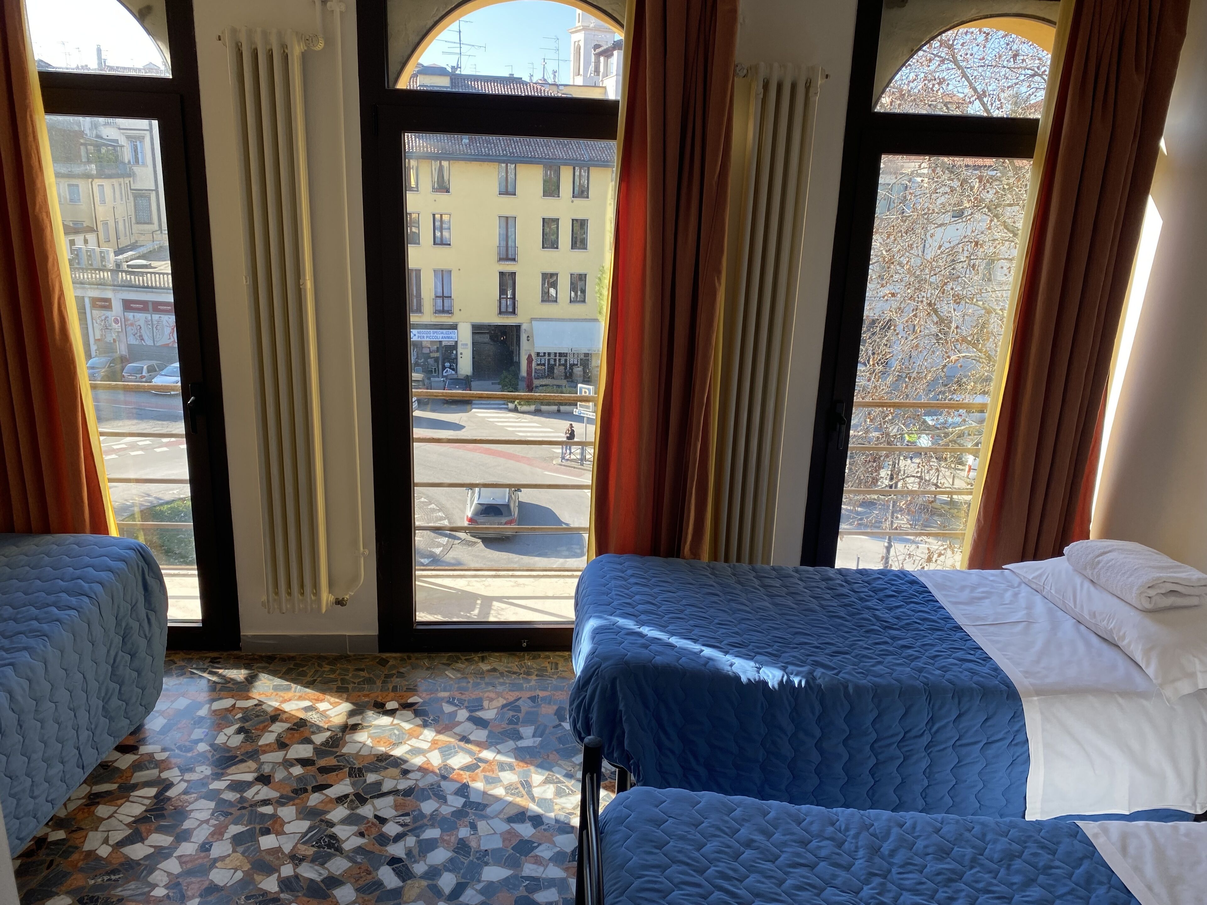 Habitación con dos camas, piso de baldosas y ventanas amplias con cortinas.