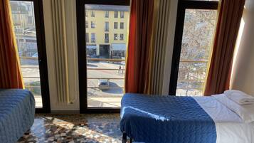 Habitación con dos camas, piso de baldosas y ventanas amplias con cortinas.