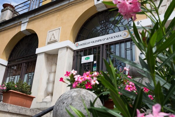 La façade extérieure de l’hôtel OSTERIA « OLIMPICO » de Vicence, avec ses fenêtres en arc de cercle et une enseigne portant le nom de l’hôtel.