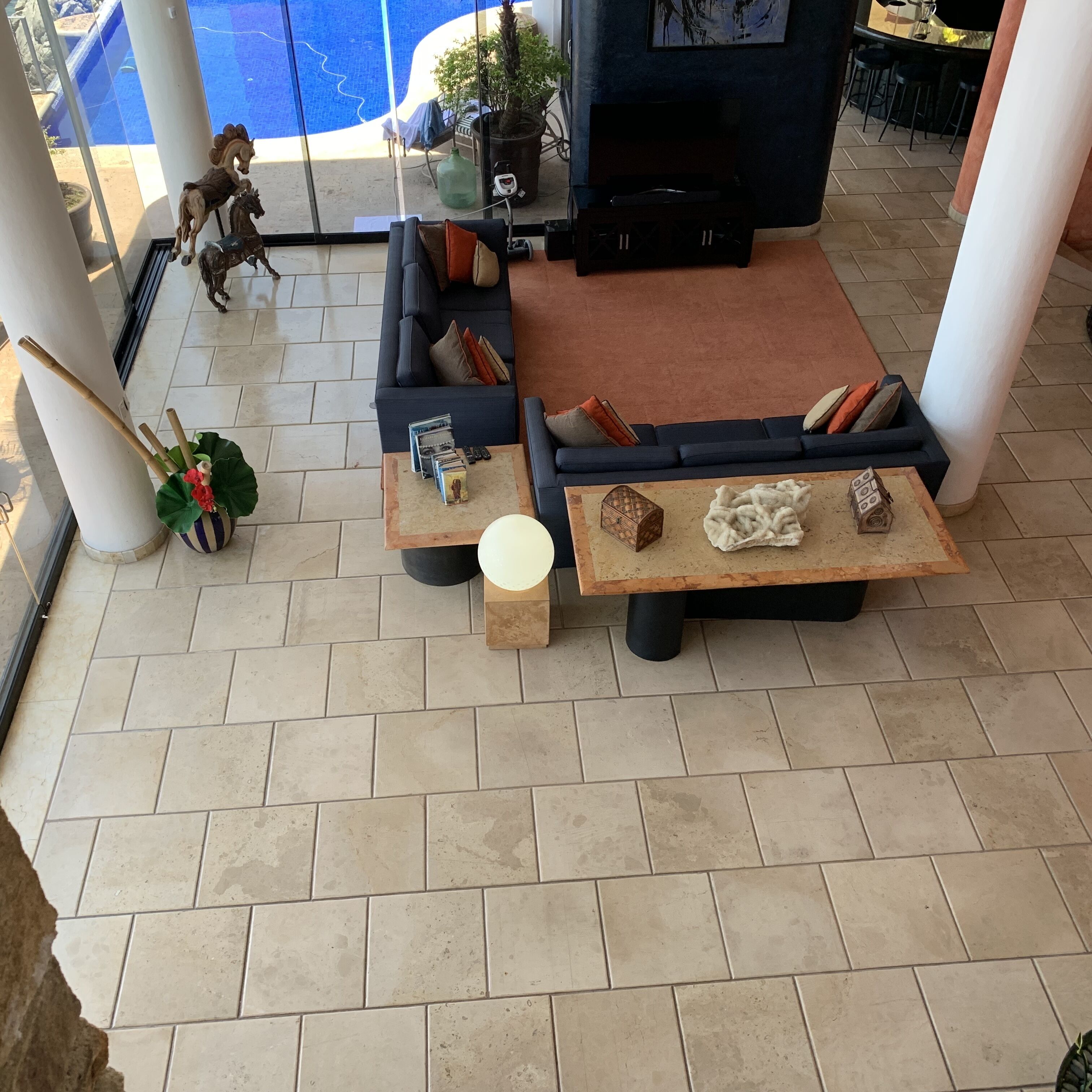Una sala de estar moderna con un sofá seccional, dos mesas de centro y un ventanal con vista a una piscina.
