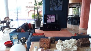 Tilava olohuone, jossa on suuri sohva, televisio ja sohvapöytä. Huoneessa on myös ruukkukasvi ja koristeellinen hevospatsas.