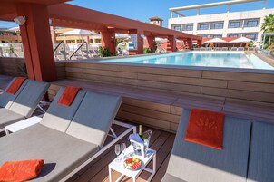 Zona junto a la piscina con sillones, una mesa con bebidas y aperitivos, y vistas a la piscina y los edificios del hotel.