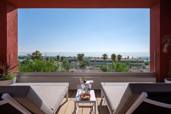 A balcony with two chairs, a table with a bottle and glasses, and a view of the sea and buildings. - Oassium Hotel at Estival Park (Vila-Seca)