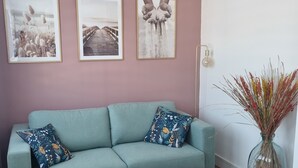 Ein Wohnzimmer mit einem petrolfarbenen Sofa, zwei runden weißen Tischen und drei gerahmten Bildern an der Wand.