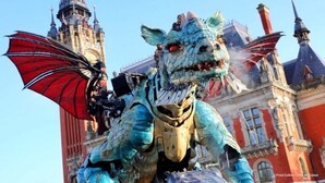 Eine Drachenstatue mit roten Flügeln vor einem historischen Gebäude mit mehreren Türmen.