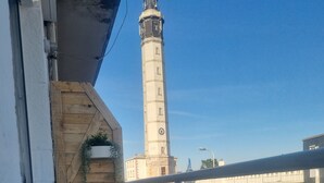 Ein Balkon mit weißem Stuhl und Tisch, mit Blick auf einen hohen Leuchtturm und moderne Gebäude.