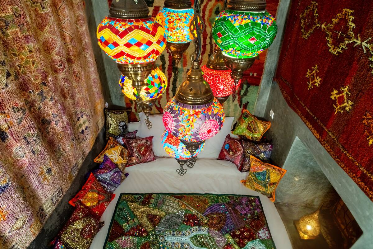 A narrow, carpeted corridor with ornate, colorful hanging lamps and a variety of patterned cushions.