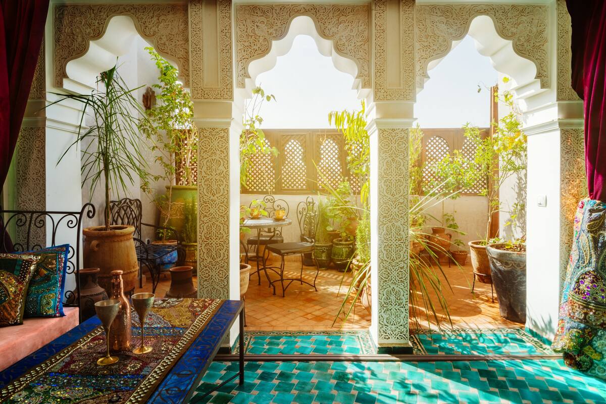 A Moroccan-style interior with a patterned floor, a seating area with cushions and a table, and potted plants.
